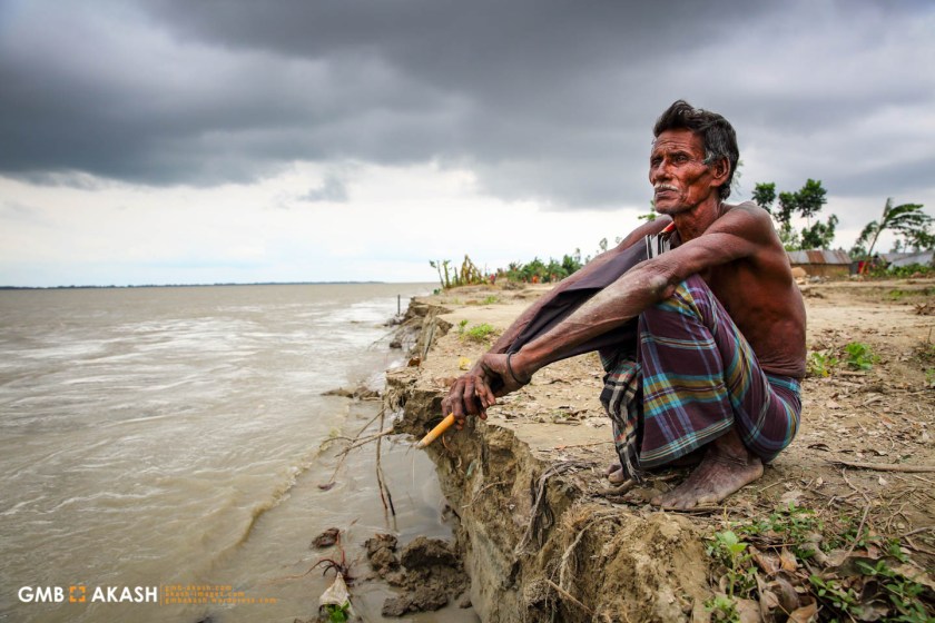 Shaha Ali (60), a resident of Sariyakandi sits on the banks of the Jamuma River where his house once stood before the eroding river banks caused it to collapse (1)